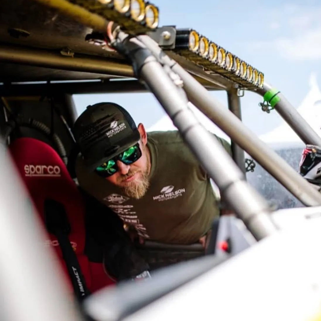 Man in a cap and sunglasses leaning into the cockpit of a race UTV with a roof light bar
