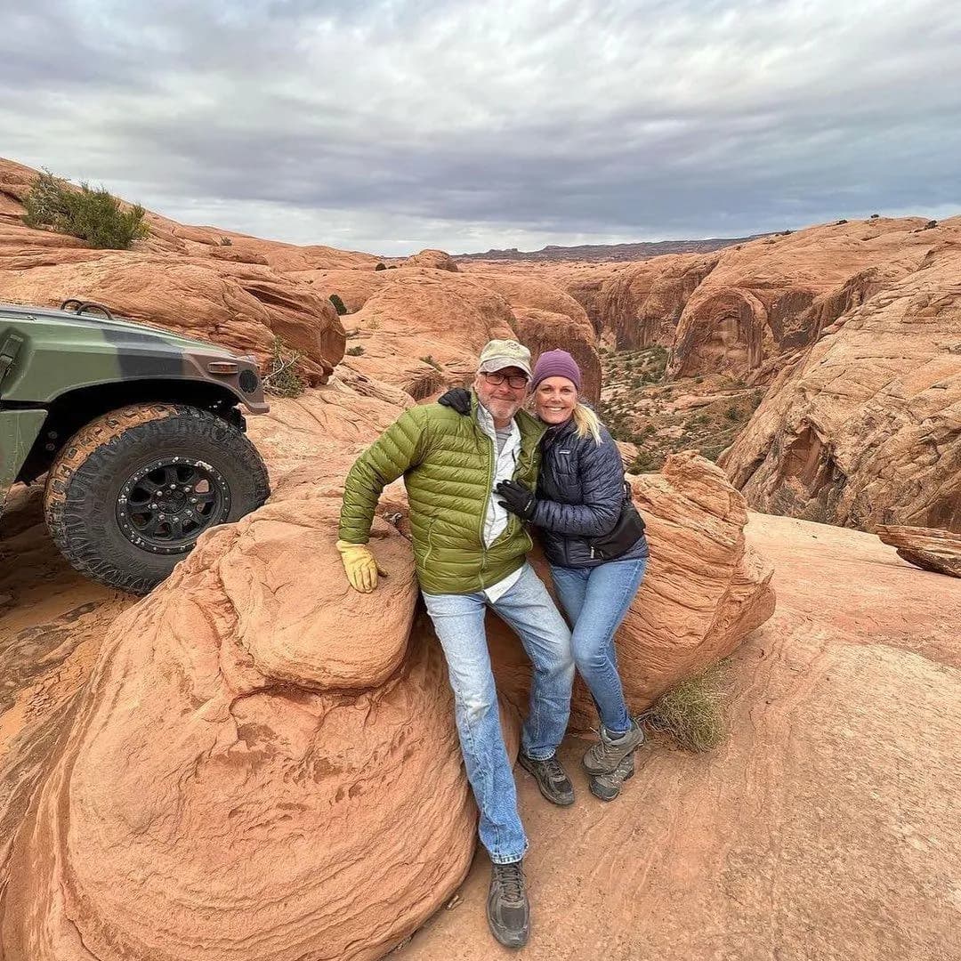 Couple sitting on a sandstone boulder beside a parked Hummer under a cloudy sky