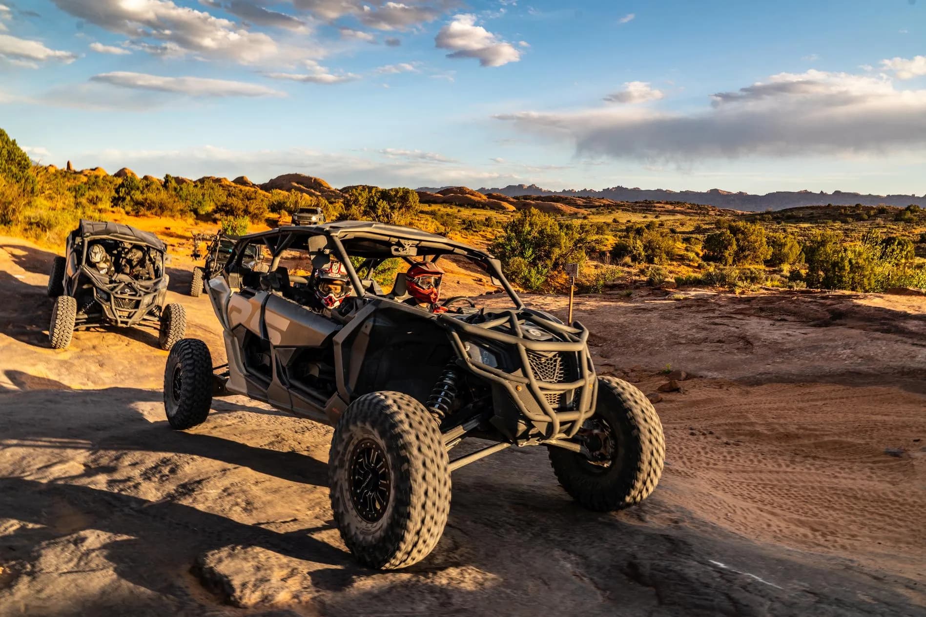 Two Can-Am UTVs parked on slickrock with desert scrub and distant mesas at golden hour