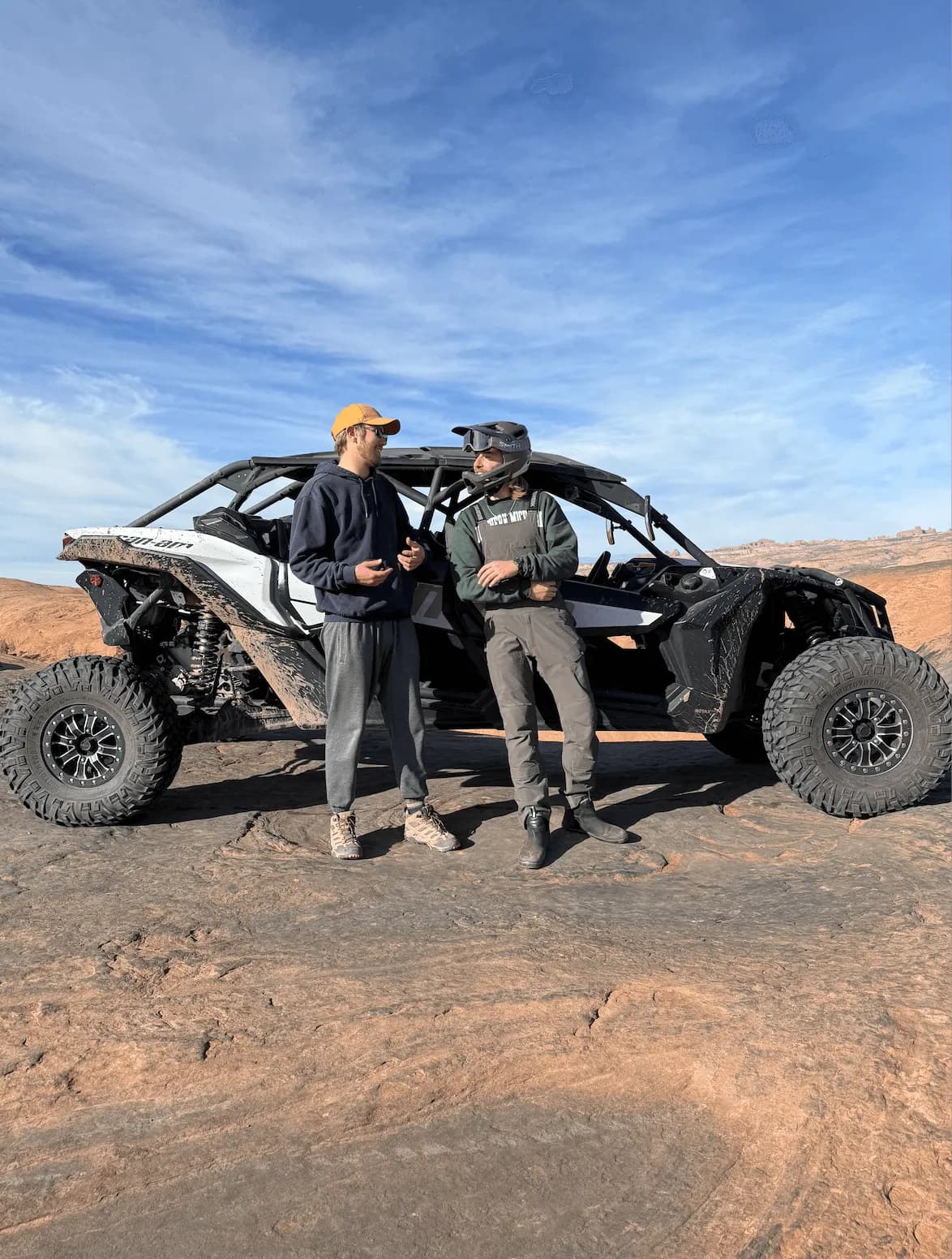 Two men standing beside a Can-Am Maverick UTV on slickrock under a blue sky