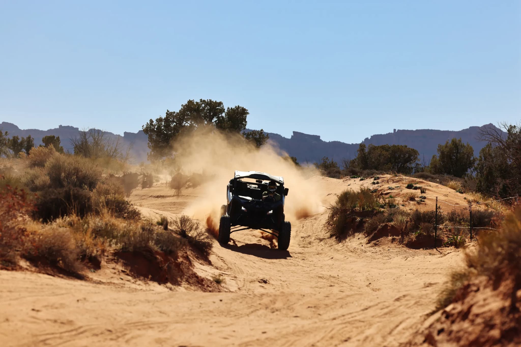 A Can-Am side-by-side throwing up a cloud of dust on a sandy desert trail
