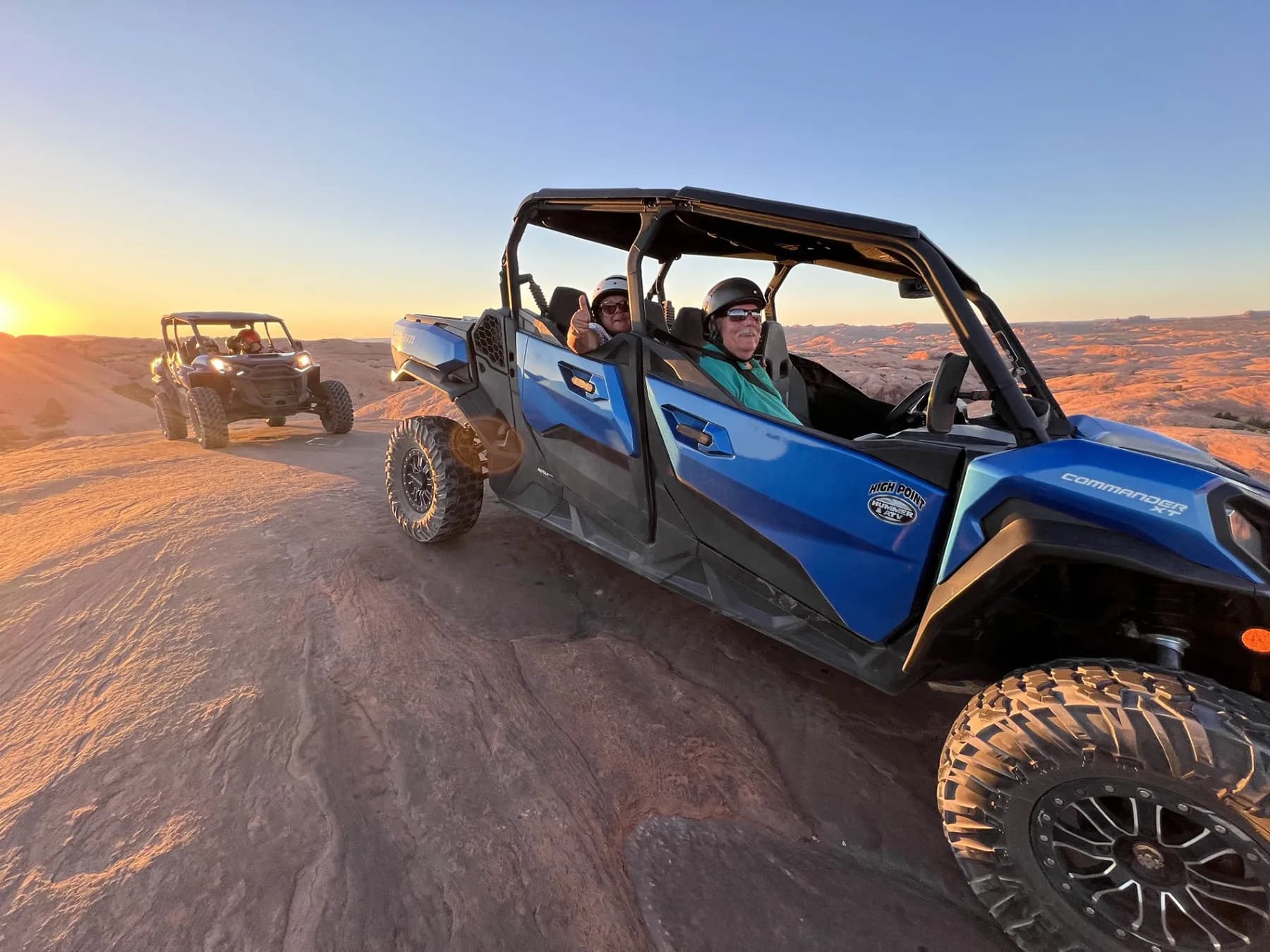Guests in a blue four-seat side-by-side on Hell's Revenge slickrock at sunset