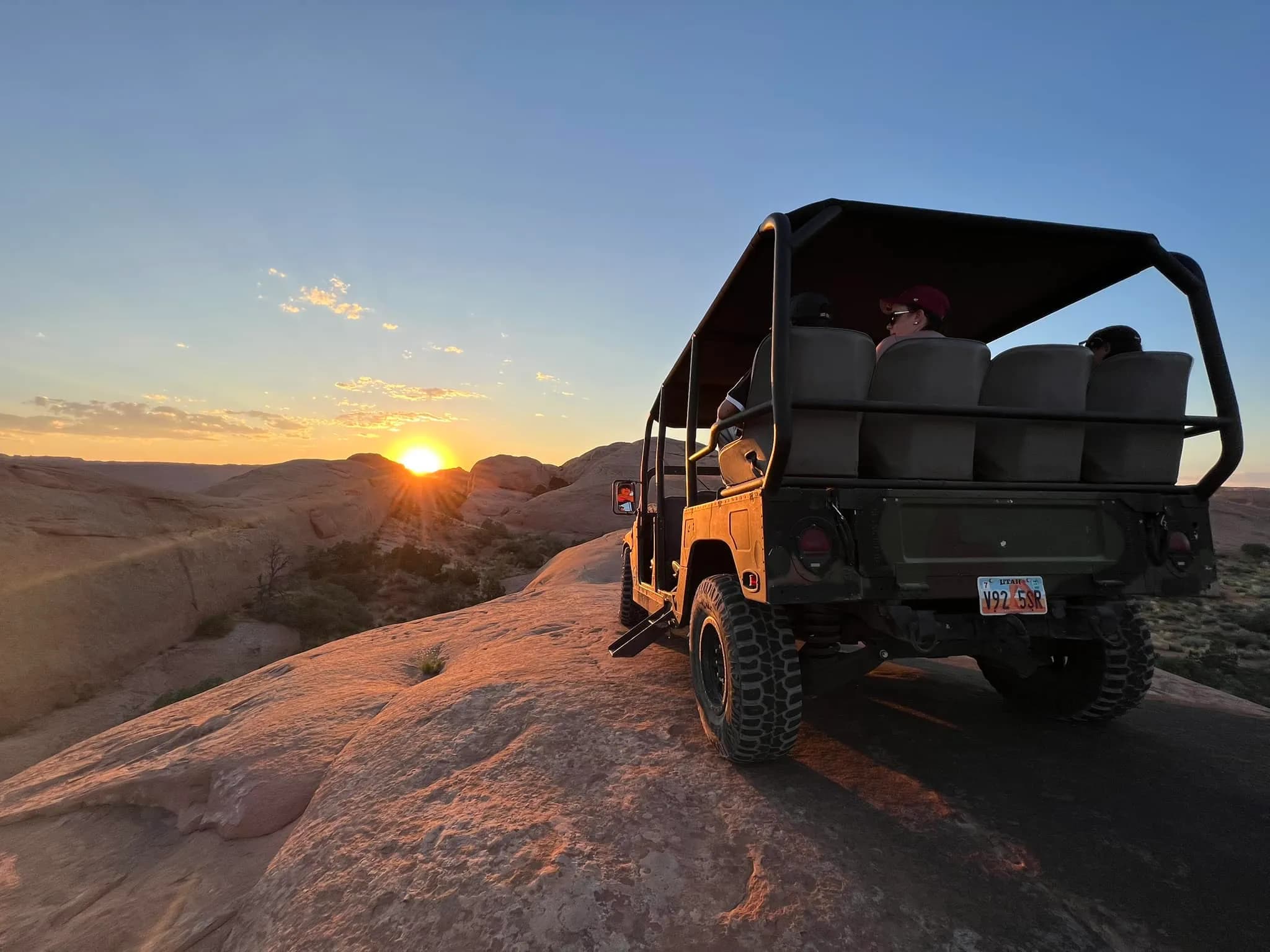 Open-top Hummer climbing a slickrock ridge toward the setting sun