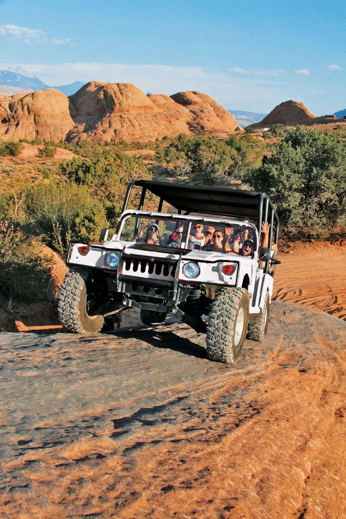 White open-top Hummer full of waving guests crawling over red rock