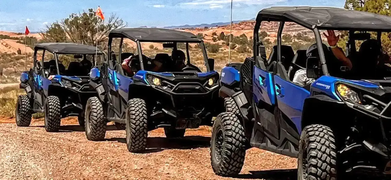 Three blue four-seat side-by-sides lined up on a red dirt trail with guests aboard