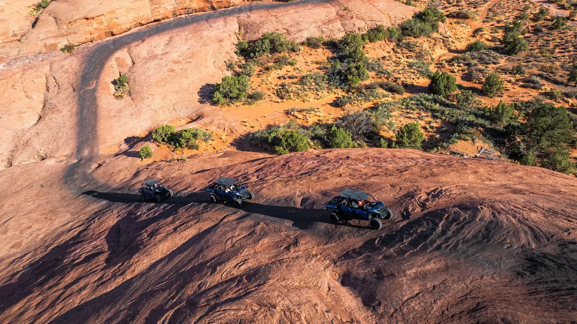 Aerial view of three side-by-sides crossing a broad slickrock slope