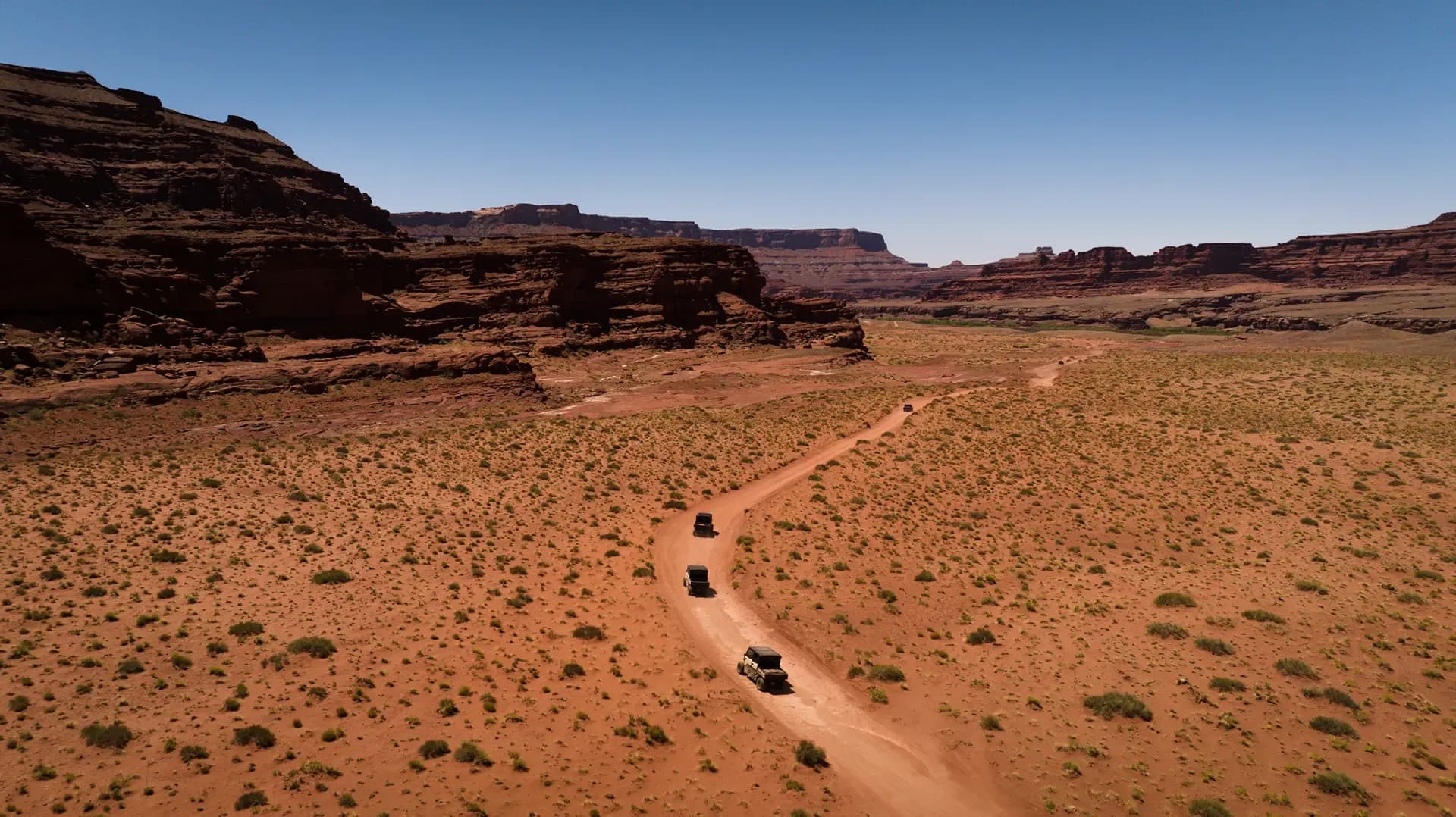 Aerial view of Hummers driving a red-rock desert trail between canyon walls near Moab