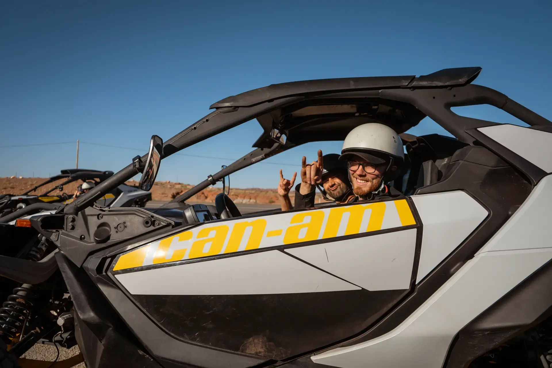 Smiling rider in a white helmet giving a hand sign from the seat of a Can-Am side-by-side