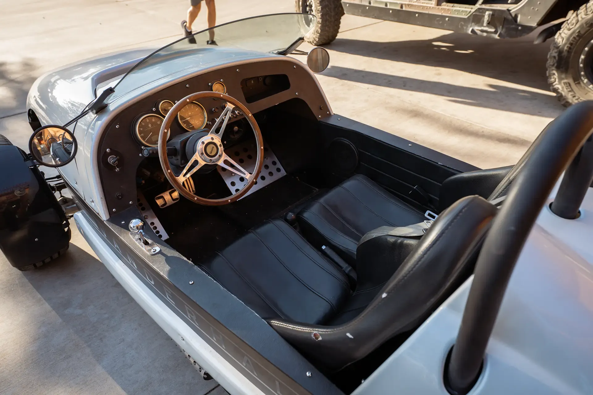 High-angle close-up view of the interior and wood-rim steering wheel of a white three-wheeled roadster.