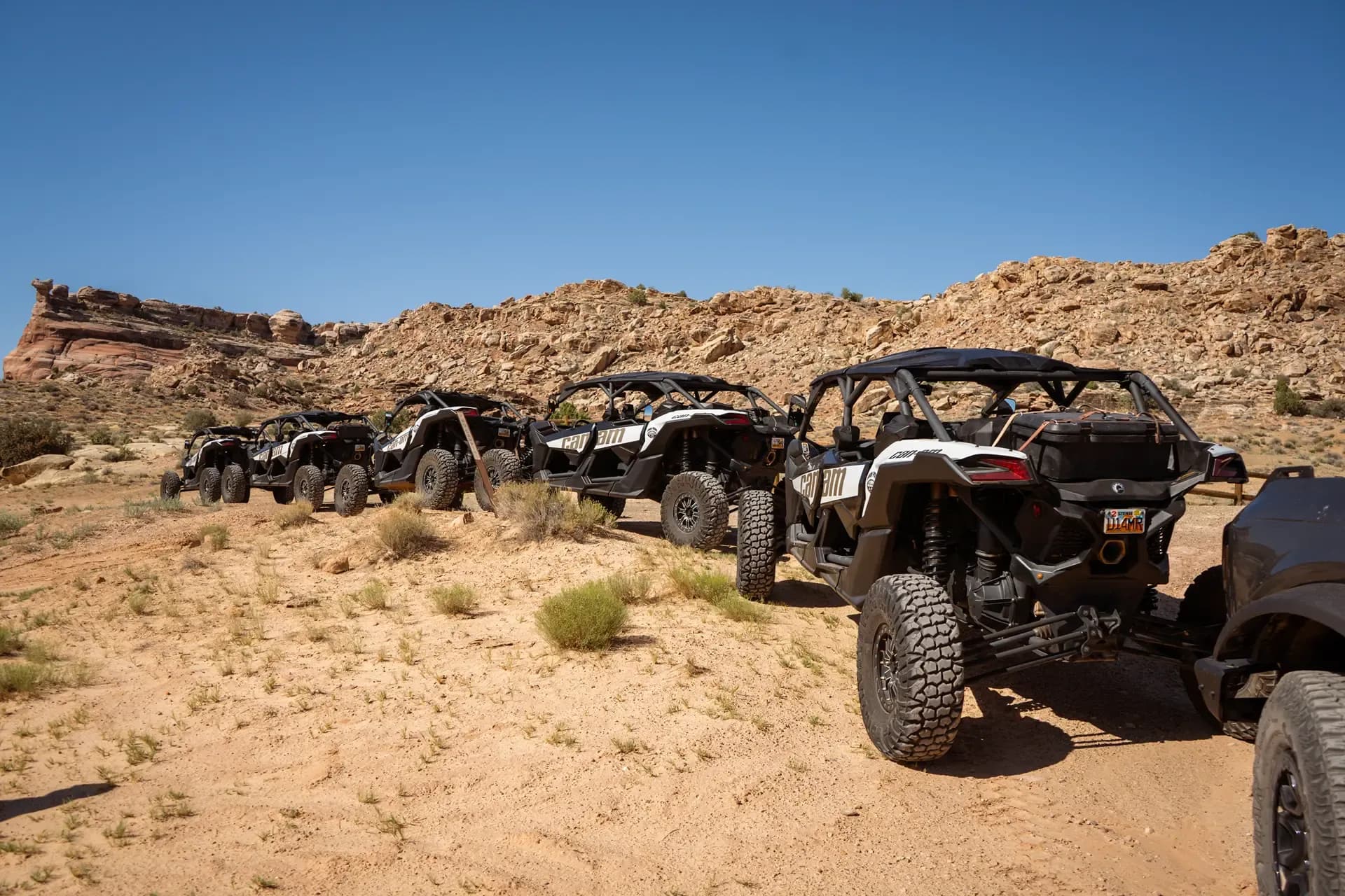 Line of Can-Am UTVs parked on a desert trail beneath sandstone cliffs
