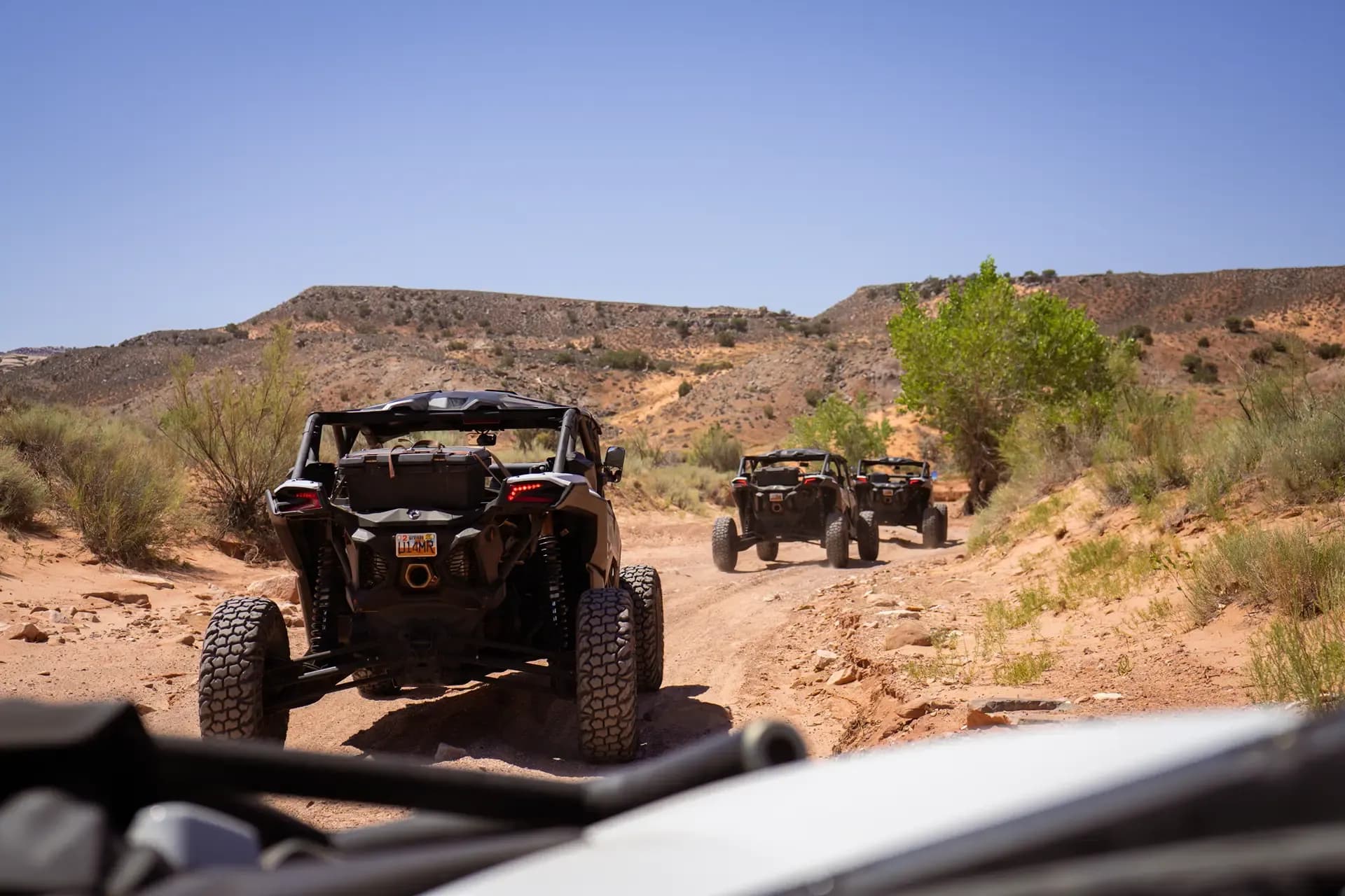 Line of Can-Am side-by-sides on a desert trail, seen from the cage of the vehicle behind