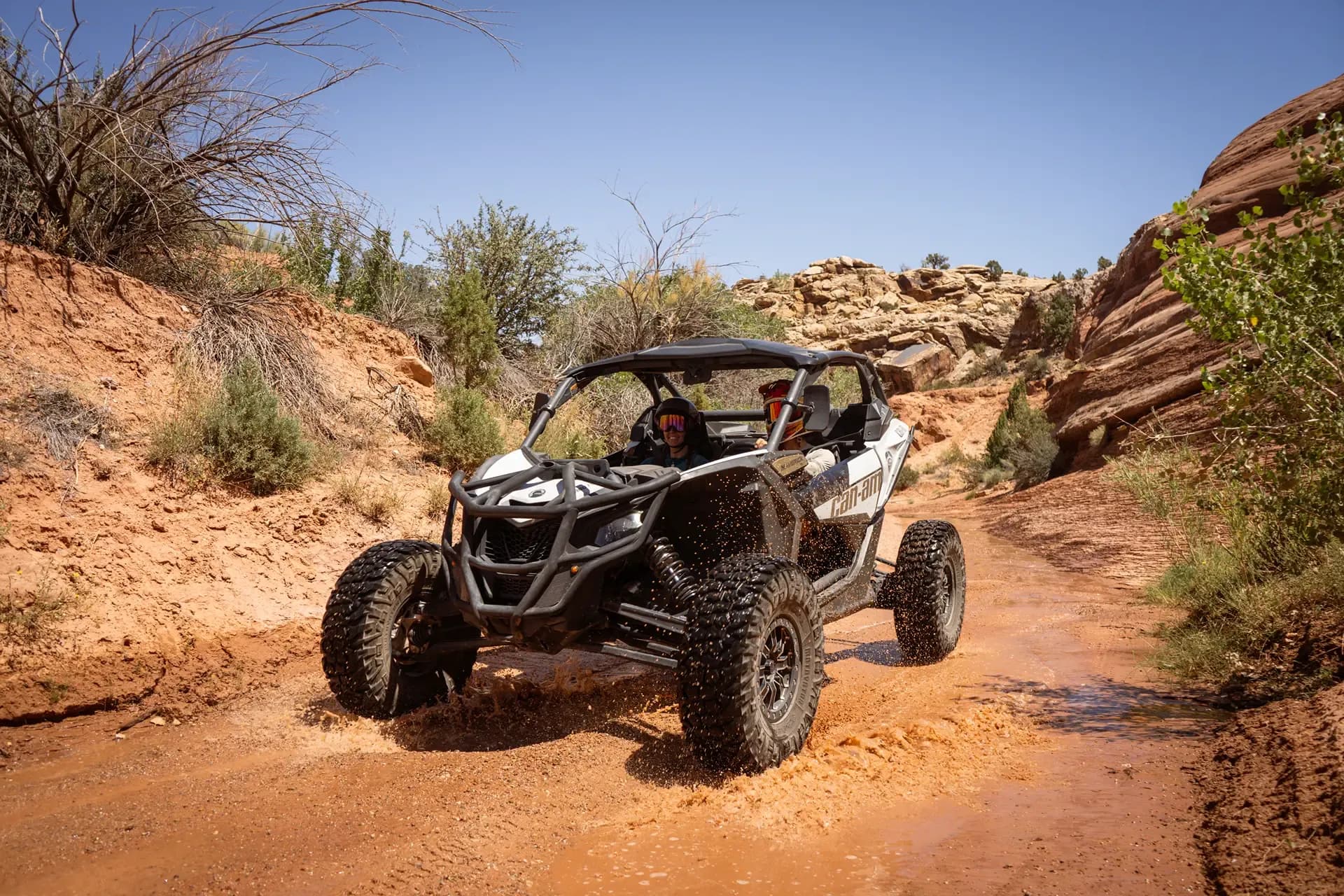 Can-Am Maverick X3 splashing through a muddy wash between red rock walls