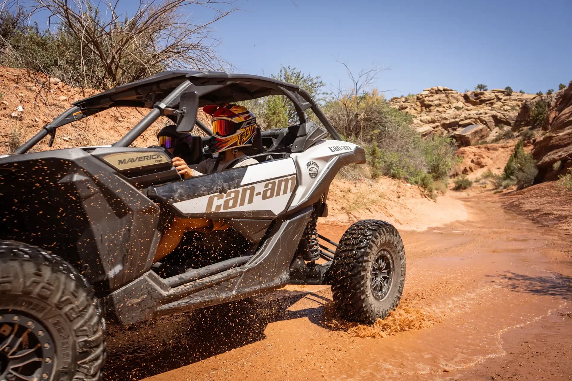 Close-up of a Can-Am side-by-side throwing mud as it splashes through a wet wash