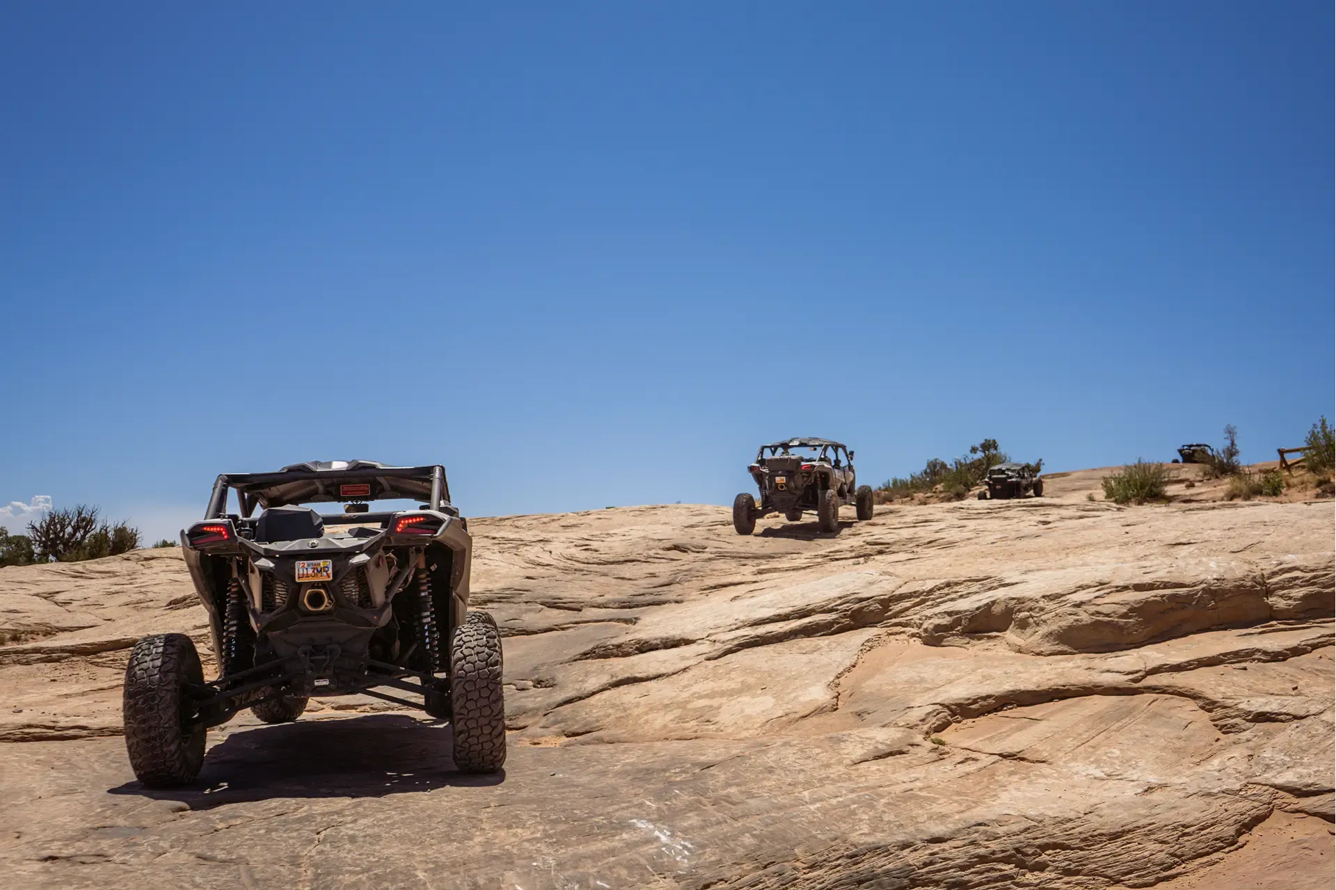 Can-Am side-by-side driving away across flat slickrock toward another vehicle