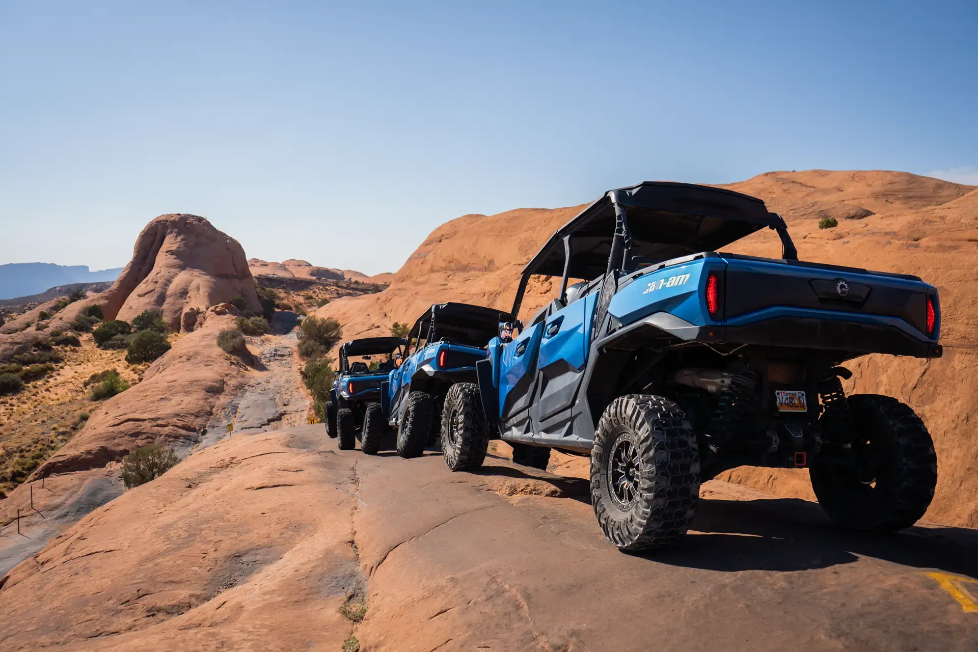 Line of blue side-by-sides parked on a slickrock ridge under a clear sky