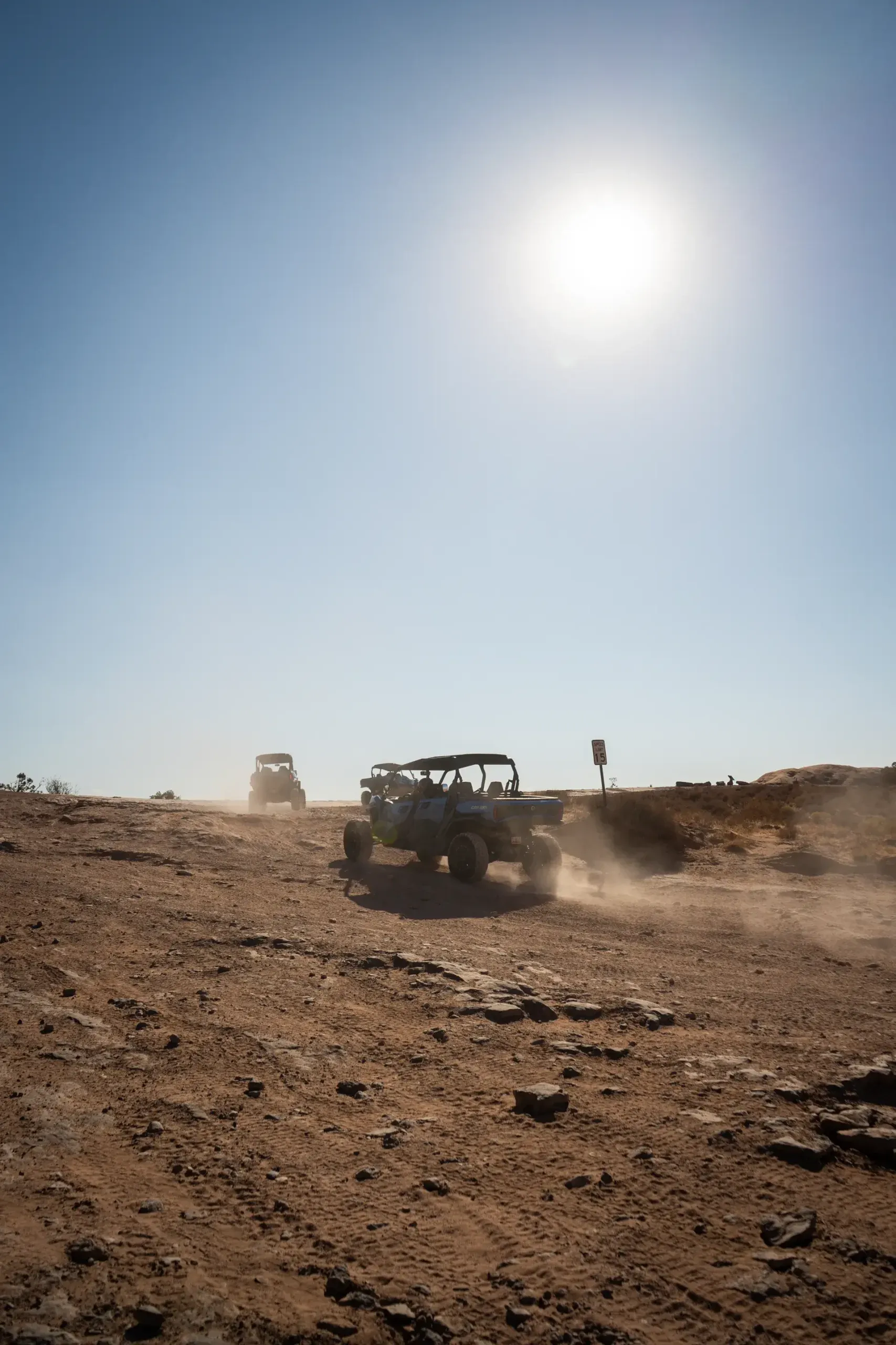 Can-Am UTVs kicking up dust on a sunlit desert trail past a 15 mph speed sign