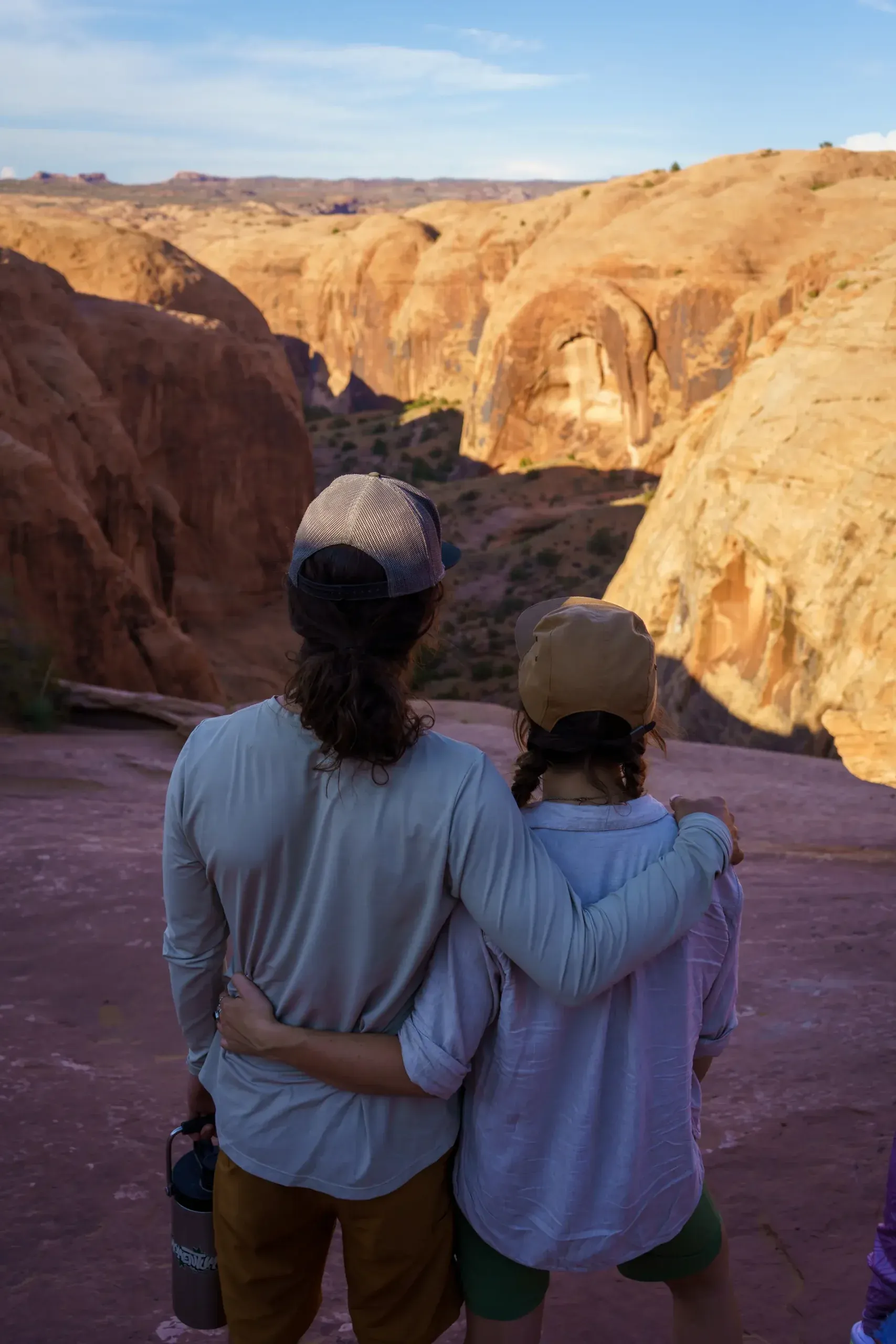 Couple with their arms around each other looking out over a sandstone canyon