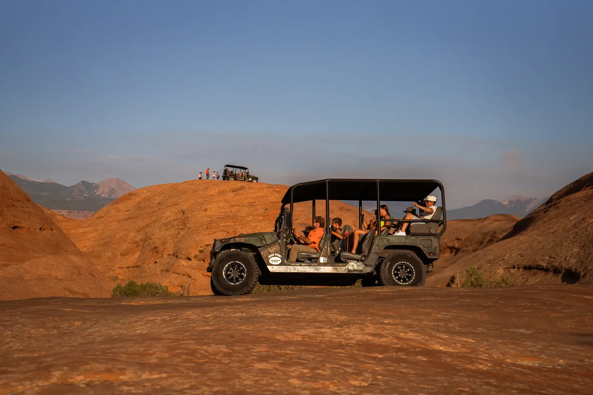 Guests in an open-top tour Hummer stopped on slickrock domes in the evening light