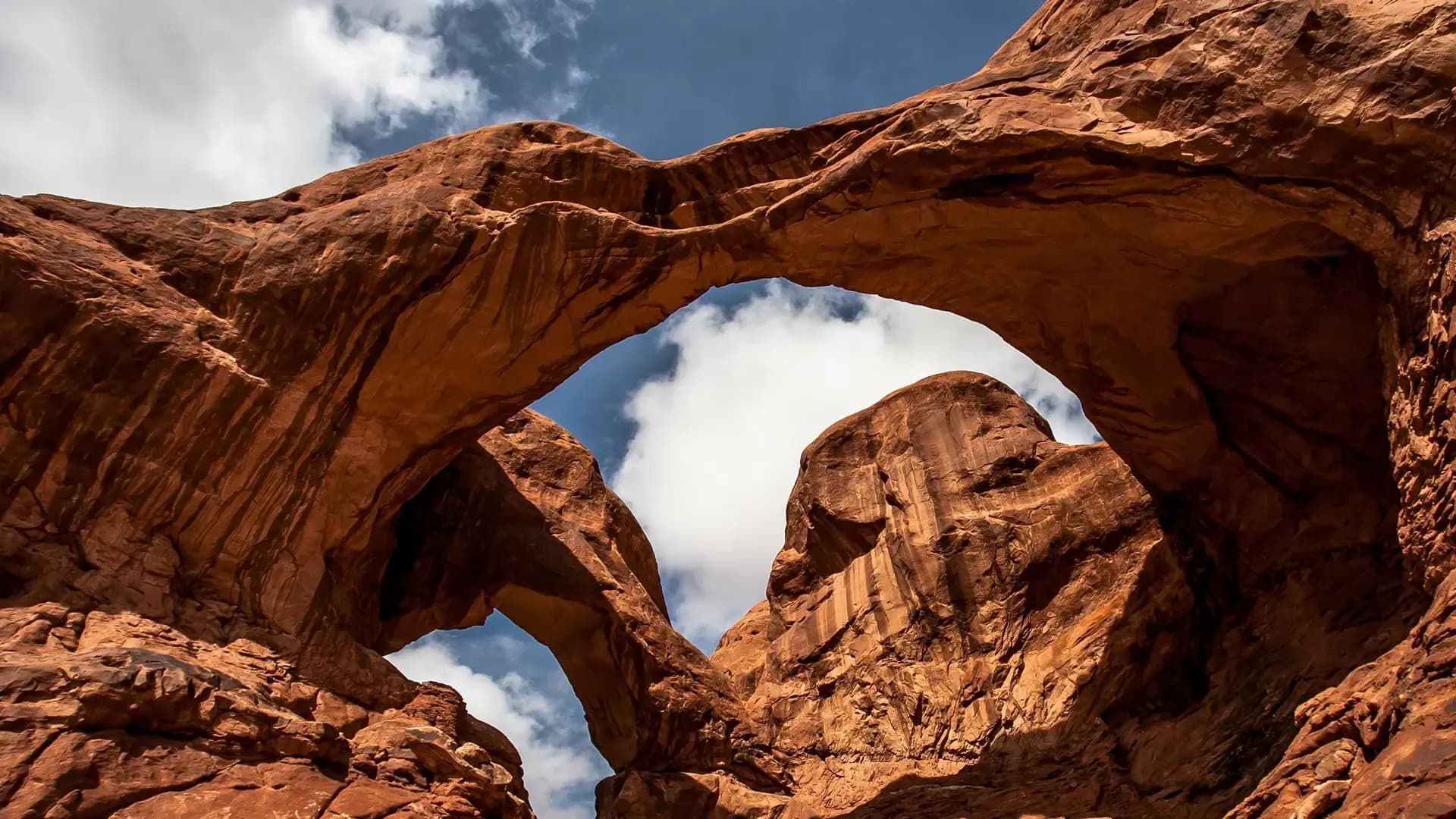 Looking up through Double Arch's red sandstone openings against a blue sky with clouds