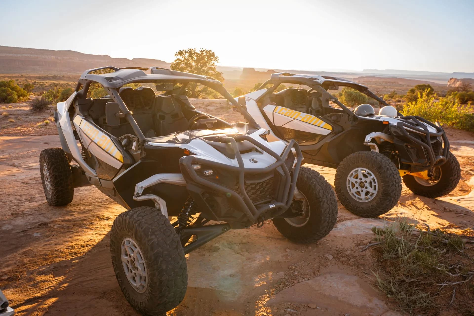 Two Can-Am Maverick R side-by-sides parked on slickrock in low golden sunlight