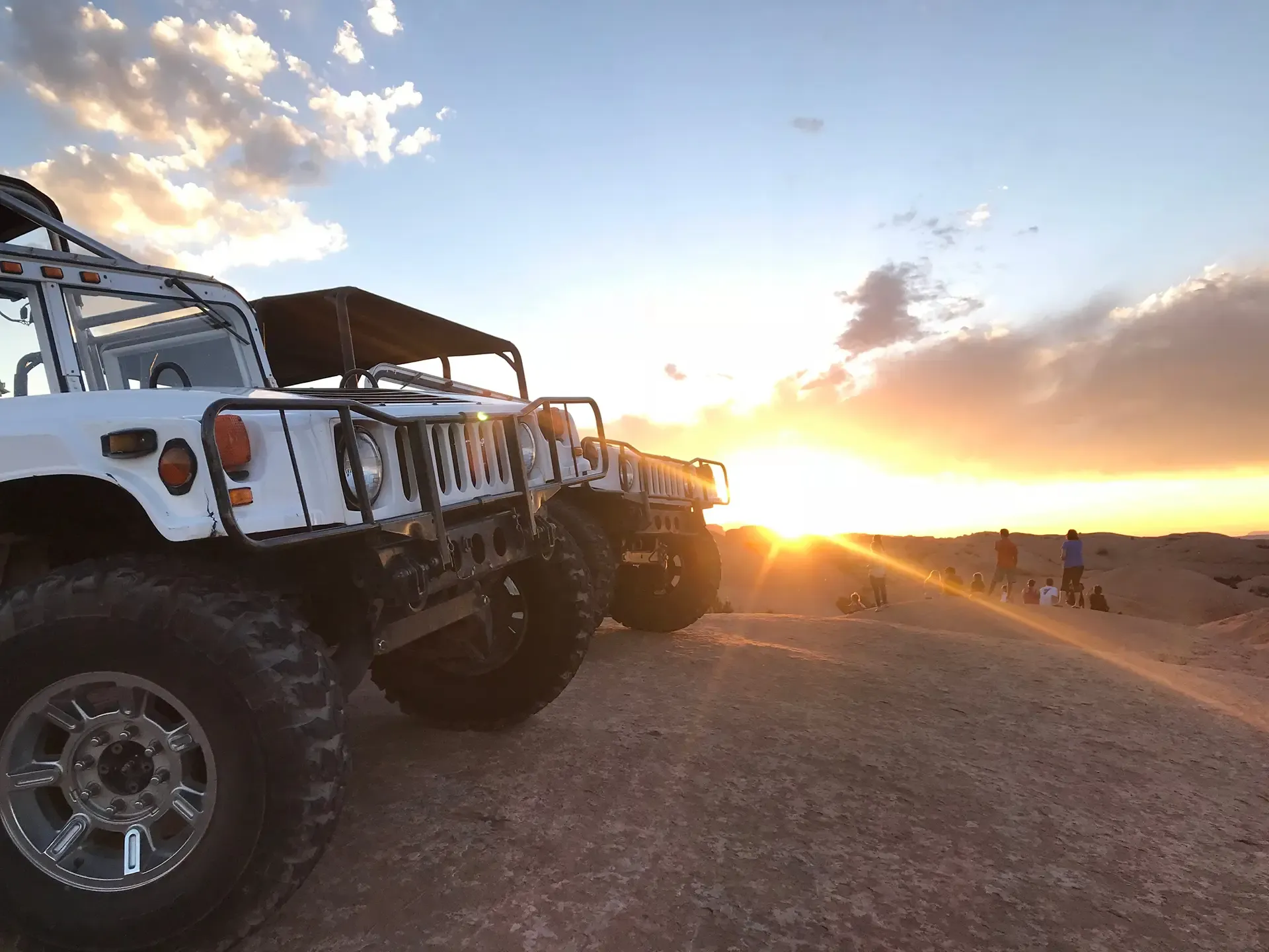 White Hummers lined up on slickrock as the sun sets on the horizon