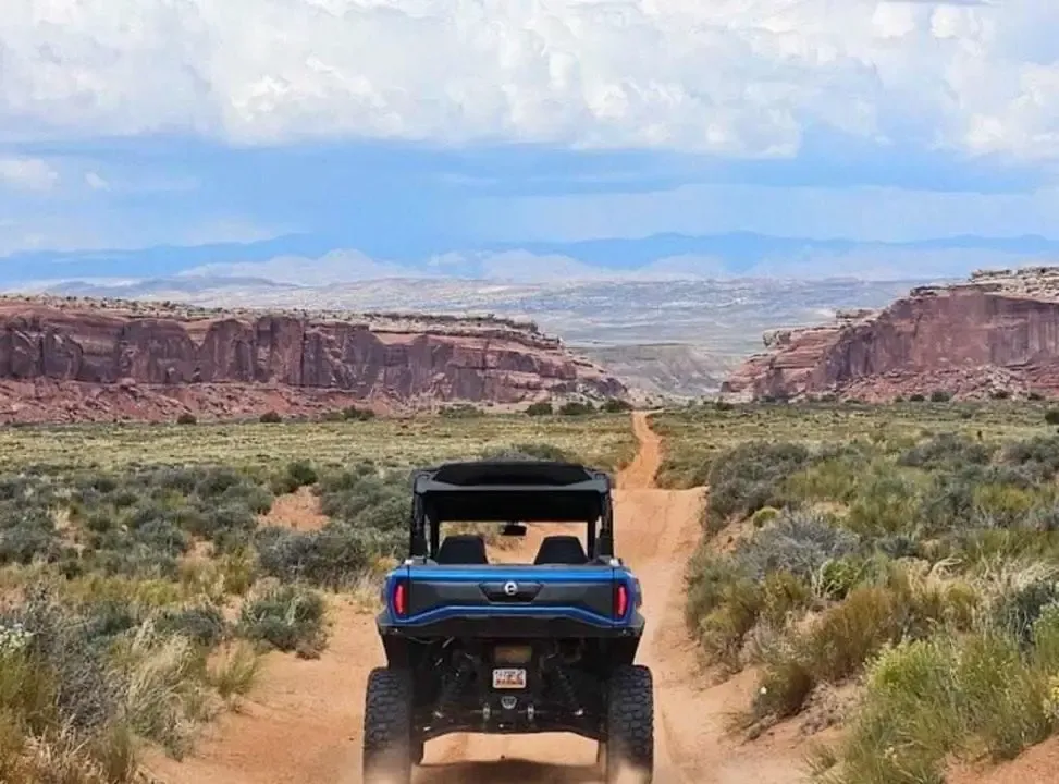 Blue side-by-side driving a straight dirt road toward a wide red rock canyon