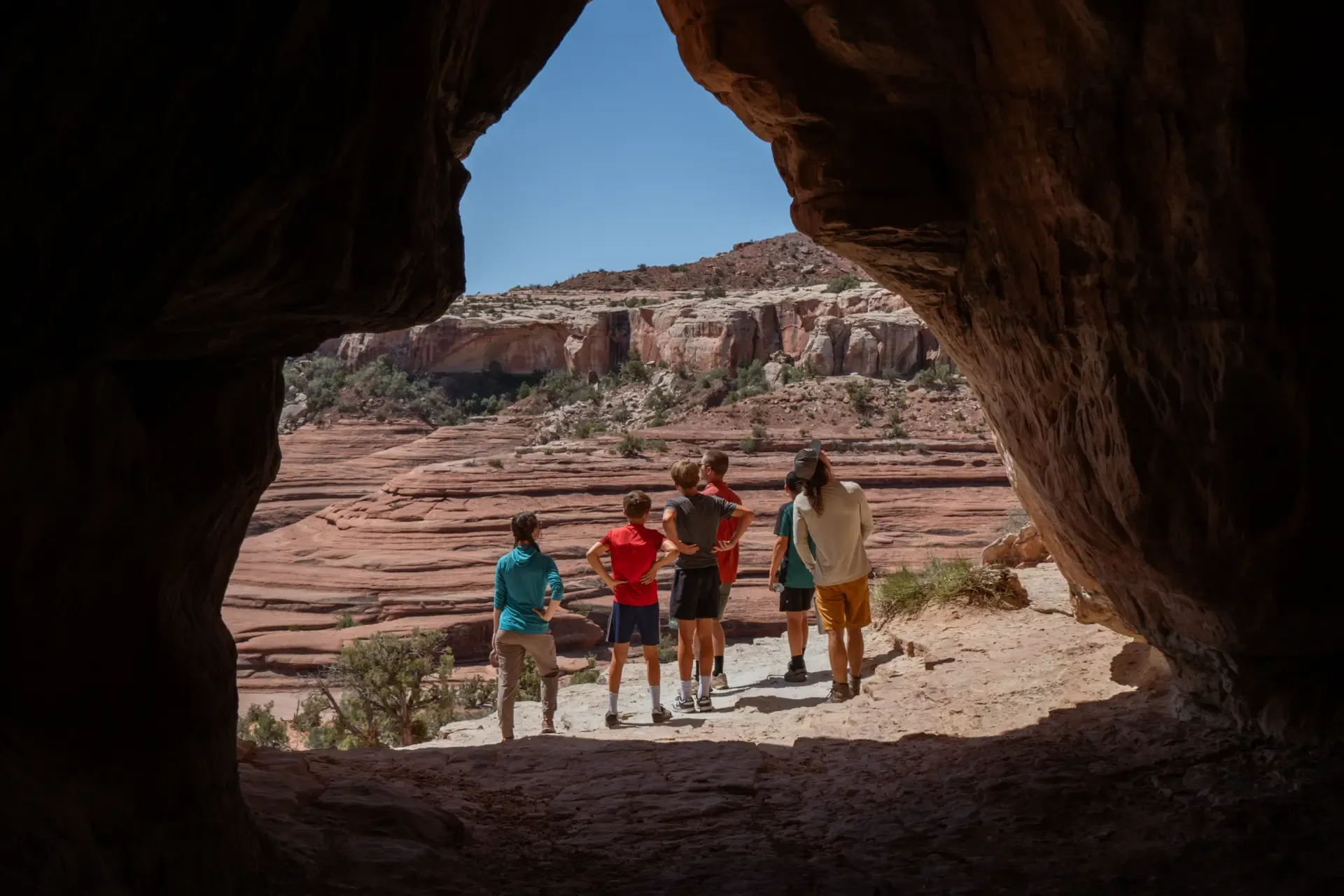 Family looking out over a red rock canyon from the shade of a sandstone alcove
