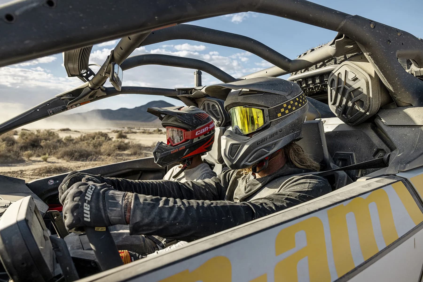 Helmeted driver and passenger strapped into a Can-Am Maverick R, close-up through the cage