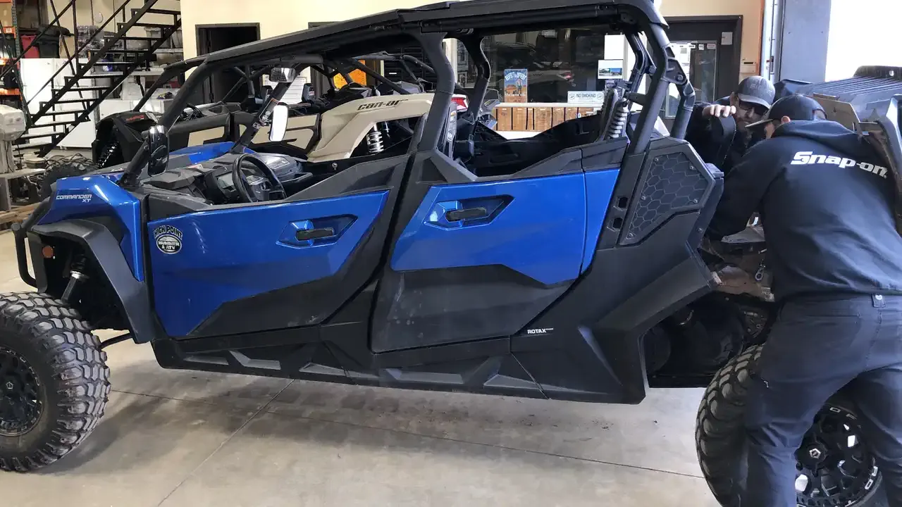 Mechanics in a Snap-on branded shop inspecting the undercarriage of a blue four-door Can-Am UTV