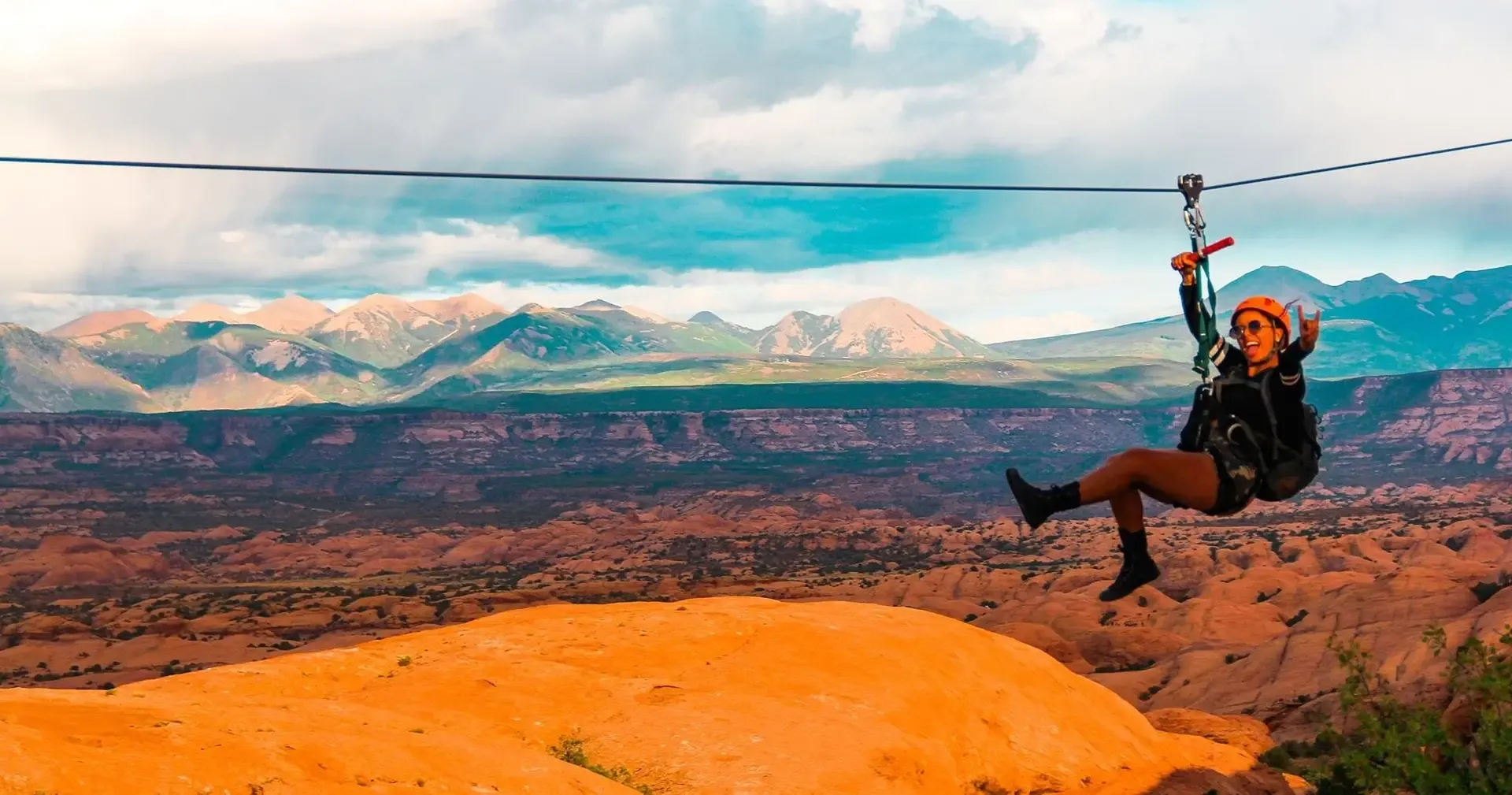 Zipliner in an orange helmet riding the cable high above the La Sal Mountains and red-rock desert