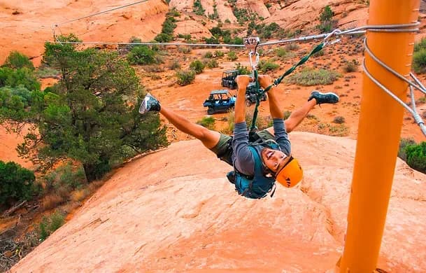 Zipliner upside down on the cable above red-rock canyon with a UTV parked below