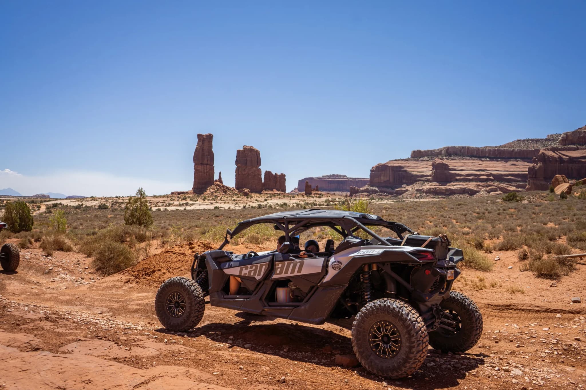 Can-Am Maverick X3 Max on a red dirt trail with tall sandstone spires in the distance