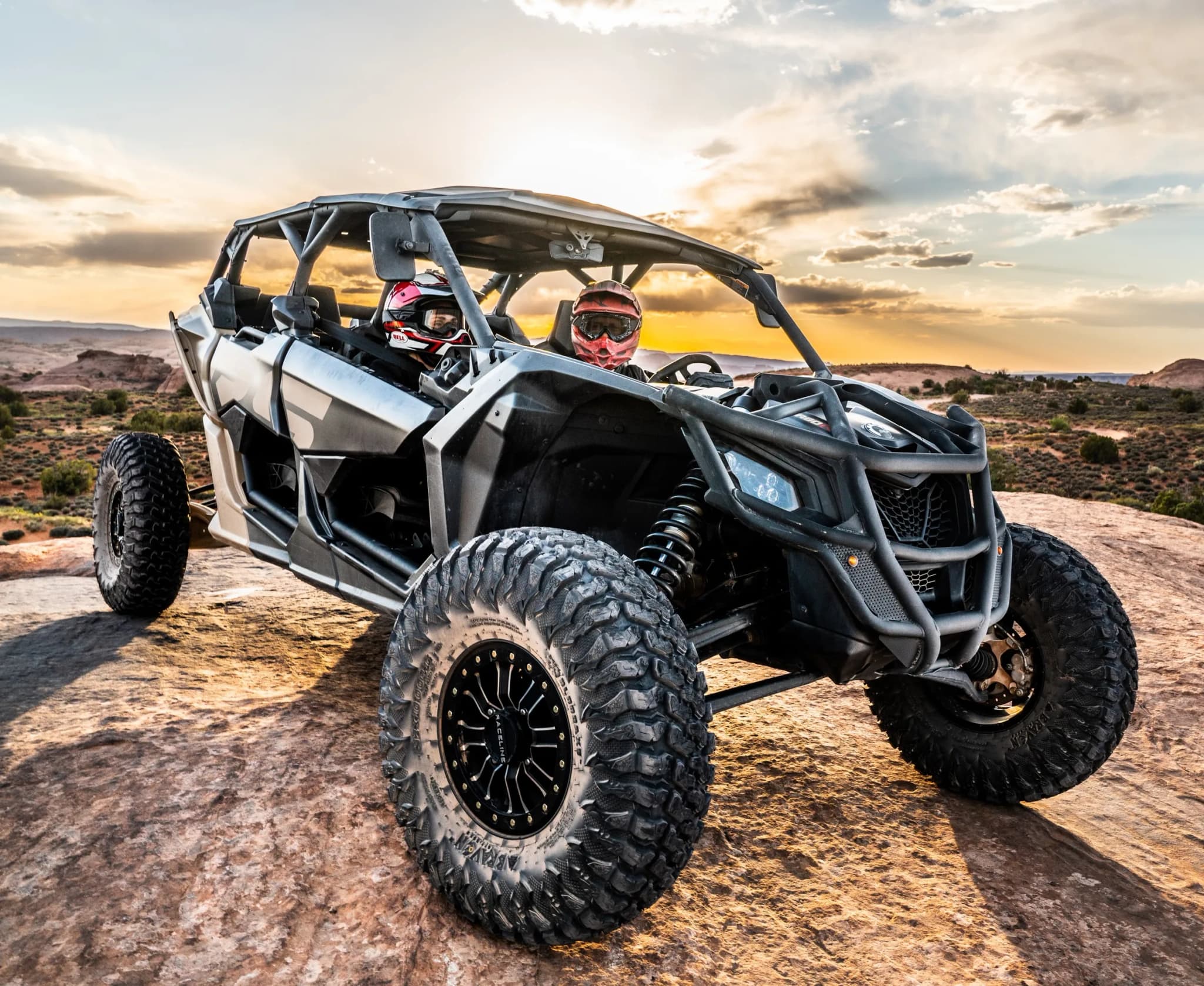 Can-Am Maverick X3 Max with two helmeted riders perched on slickrock at sunset