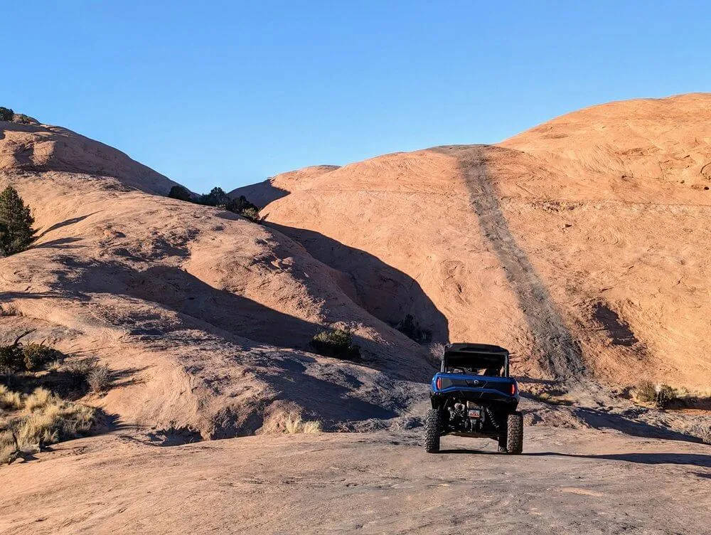 UTV parked at the foot of a steep slickrock climb under a clear blue sky