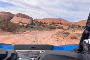 Driver's-seat view across a sandy slickrock trail from a blue UTV