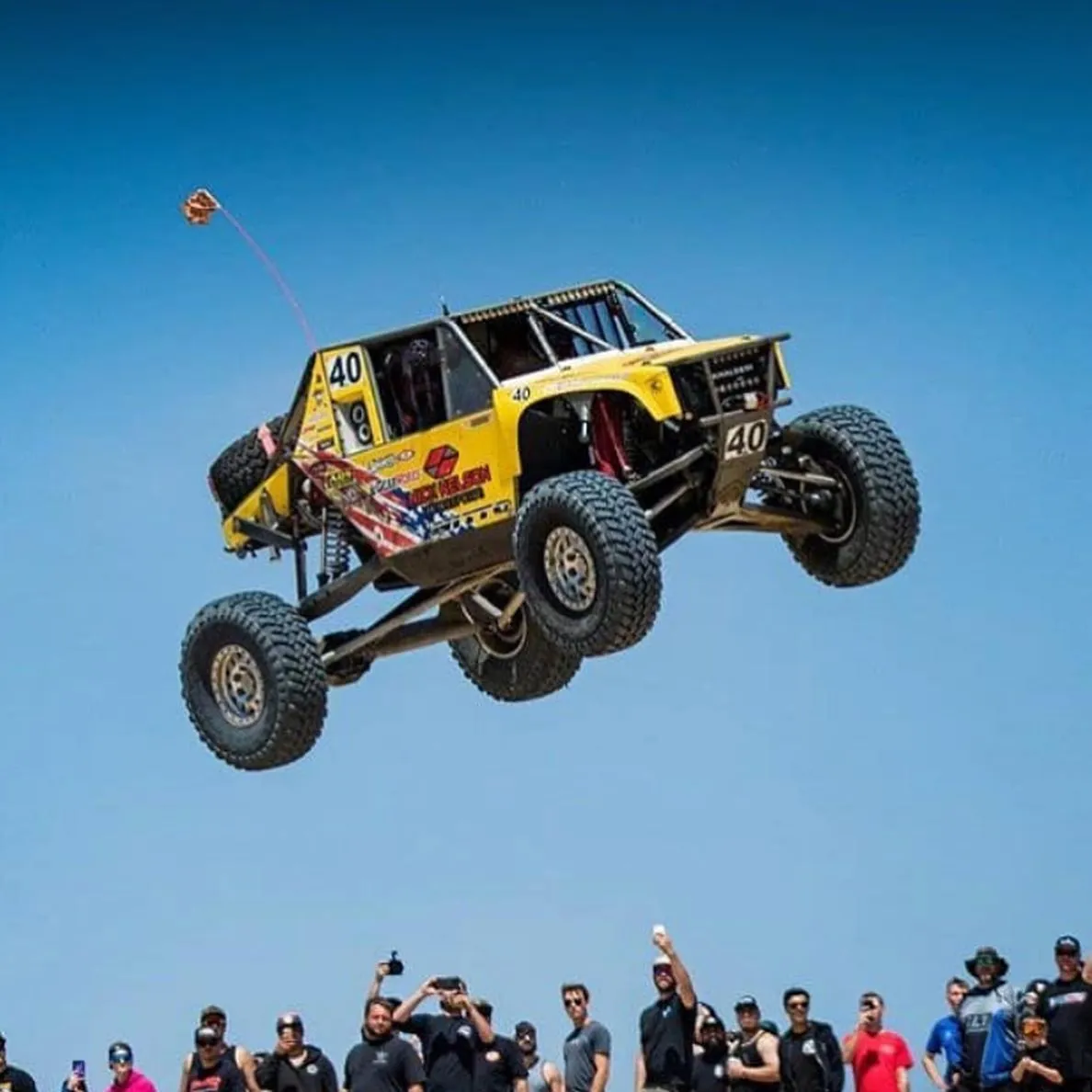 Yellow rock-crawler race buggy jumping high in front of a crowd
