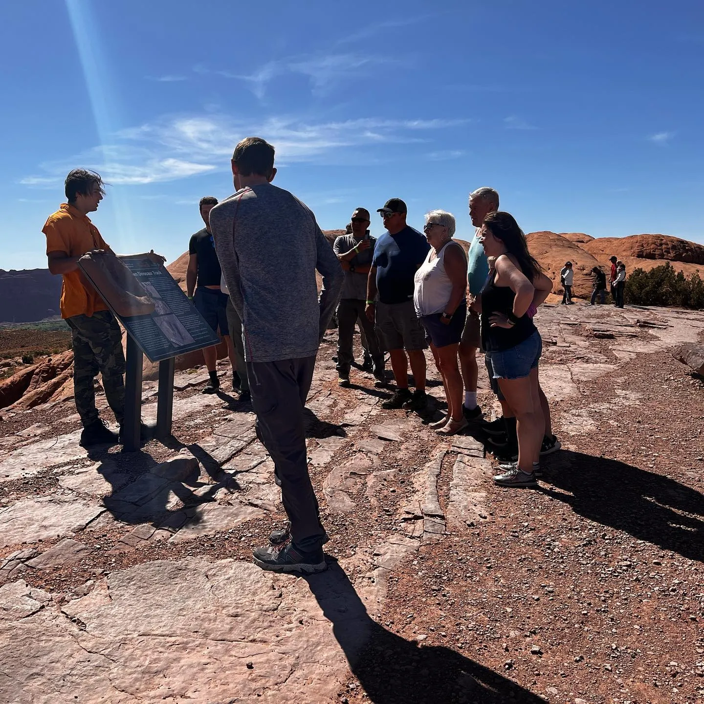 Guide and guests gathered around a trailside interpretive sign on open slickrock