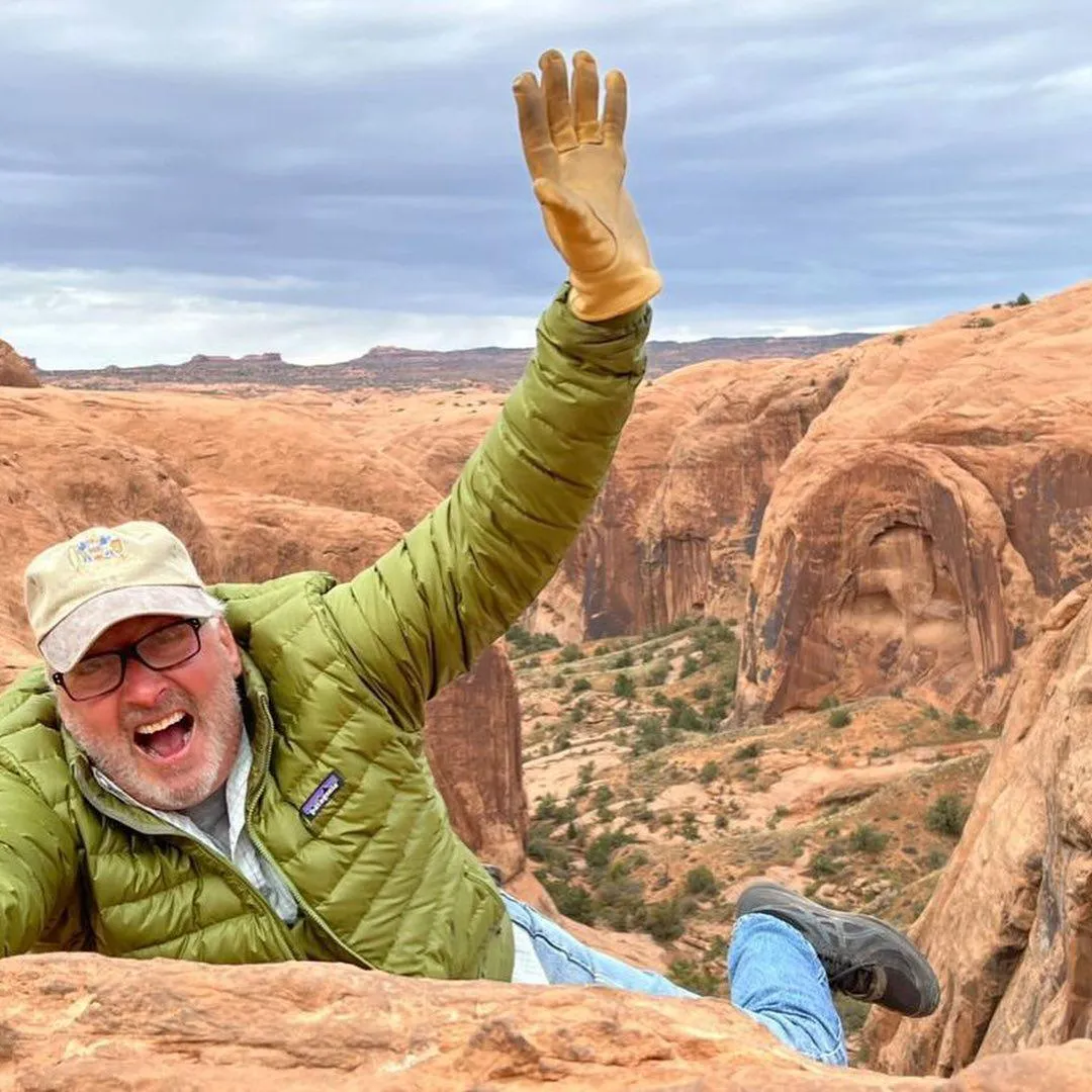 Guest in a green jacket waving excitedly from a slickrock ledge
