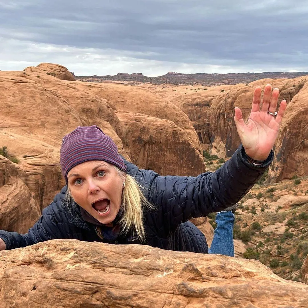 Guest in a purple beanie waving from the rim of a slickrock bowl