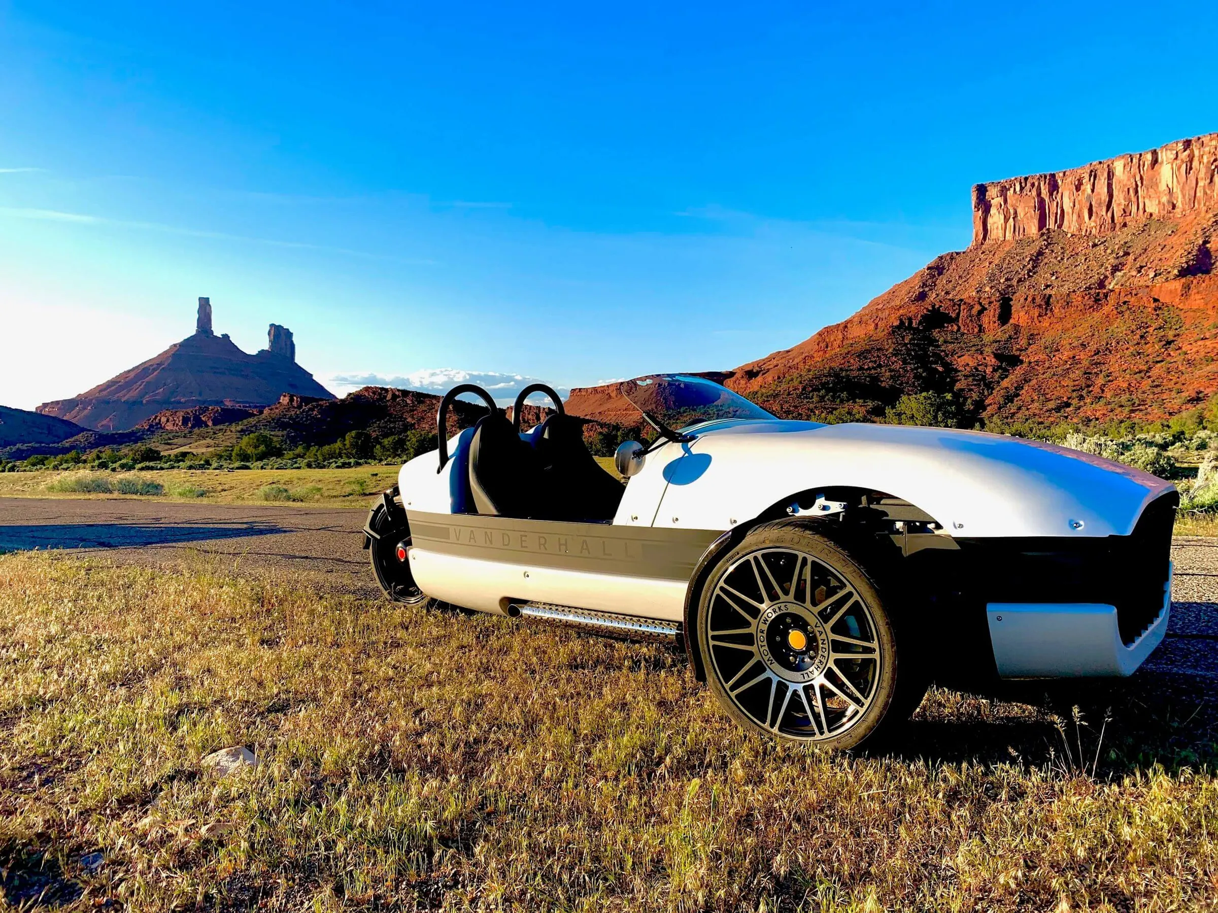 White Vanderhall three-wheeler parked in a meadow below red-rock towers