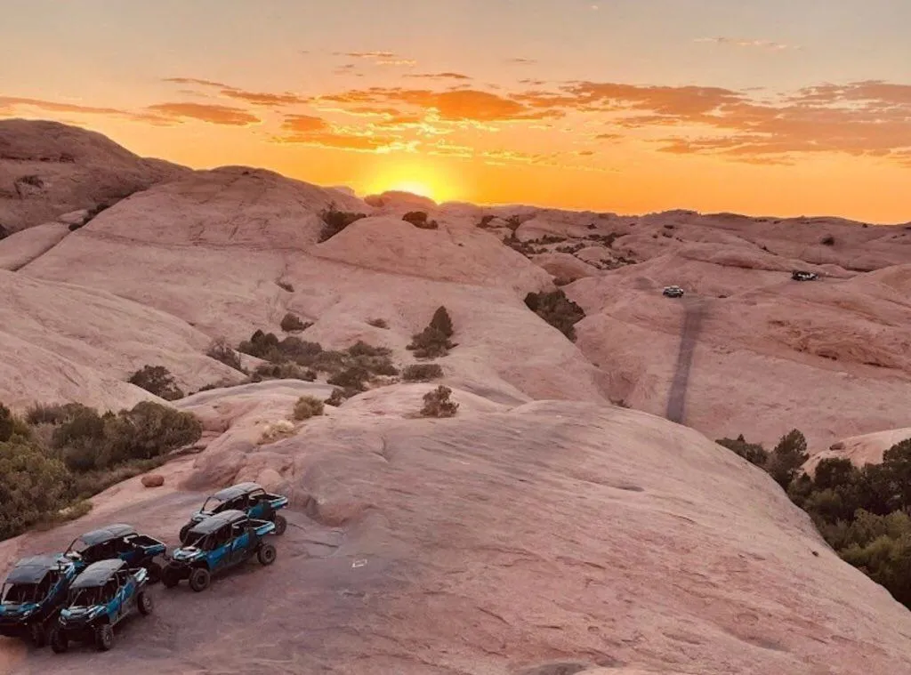 Several UTVs parked on rolling slickrock as the sun sets over the desert