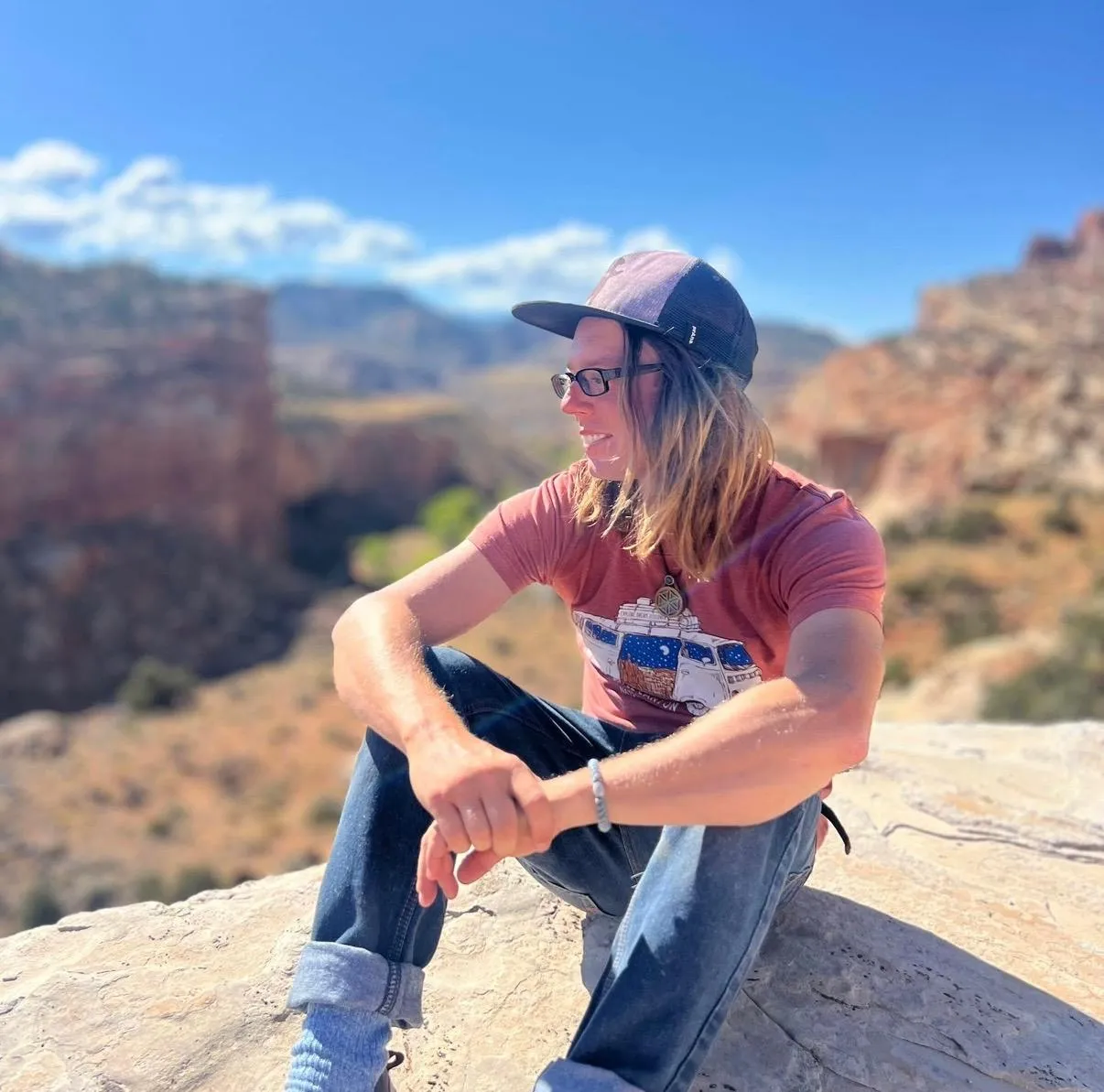 Guide JP sitting on a red-rock ledge above a canyon