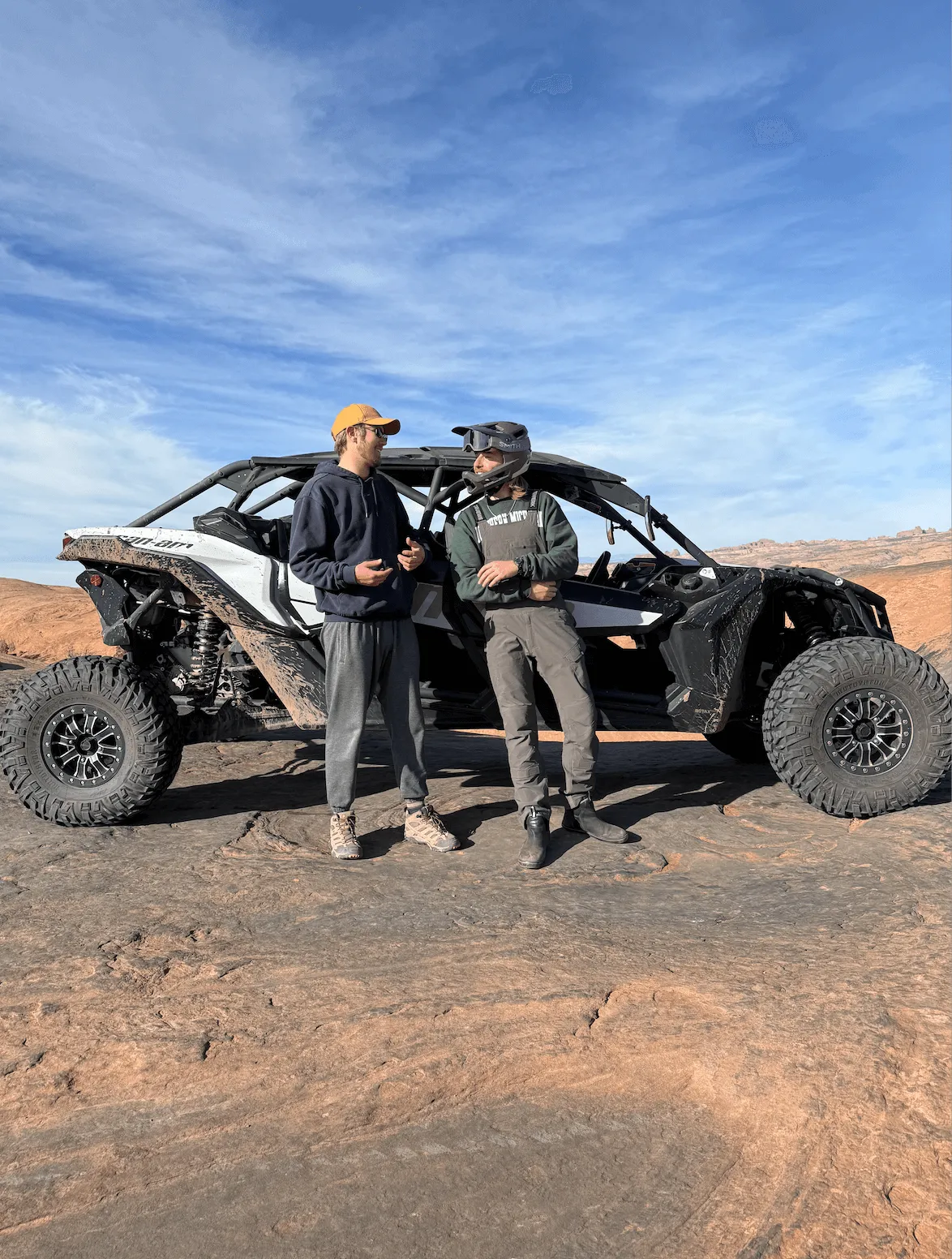 Two men standing beside a Can-Am Maverick UTV on slickrock under a blue sky